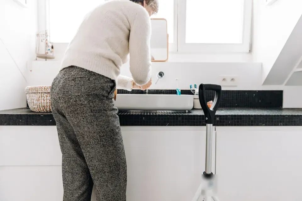 Personne âgée au lavabo, canne à portée de main
